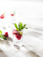 Raspberry vodka glass shot with fruit inside. Fresh summer shots for party. Berries in alcohol glass. Glass of sparkling water.