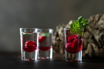 Raspberry vodka glass shot with fruit inside. Fresh summer shots for party. Berries in alcohol glass. Glass of sparkling water.