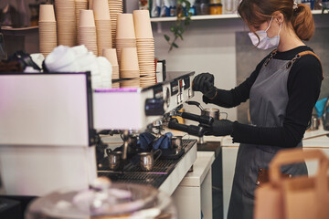 Busy female barista operating coffee machine and making hot beverage