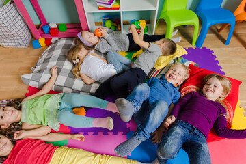 Active kids laying on soft pillows and mats at the kindergarten