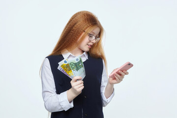 attractive red-haired girl is holding euro banknotes and a smartphone.