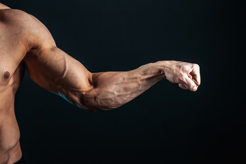 tense arm clenched into fist, veins, bodybuilder muscles on a dark background, isolate