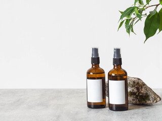 Two brown glass bottles with white label, stone and green plant leaves