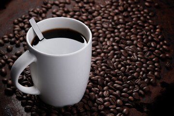 black coffee in white mug with surrounded by roasted coffee beans on dark red wood table