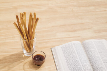 breadsticks in transparent glass with ketchup and opened page of a book on wood table