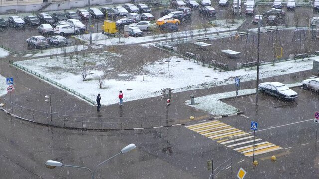 Snowfall in the city in spring (April). Top view from the window to multistorey buildings, street, playground and courtyard.