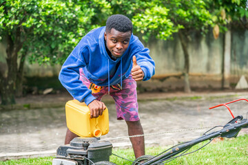 image of african guy with yellow gallon fueling a mower-  thump up sign- gardening concept