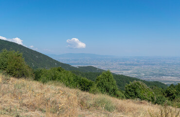 A view from an elevated position to the valley, meadows and agricultural land. Blue sky with white cumulus clouds. Summer time. Horizontal photo. 
