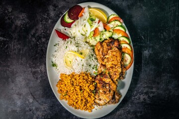 Grilled Chicken with Rice, Salad, Grilled tomato, Garnished with lemon Turkish restaurant dish isolated black granite background 