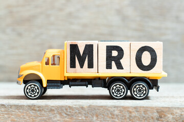 Toy truck hold alphabet letter block in word MRO (Abbreviation of Maintenance, repair and overhaul or Maintenance, Repair and Operations) on wood background - obrazy, fototapety, plakaty