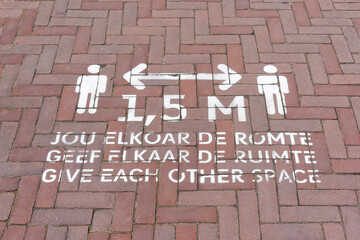Social distancing sign painted on the street to advise pedestrians to keep 1,5 meters apart during the coronavirus covid-19 pandemic. Sign with text in the frisian, dutch and english language.    