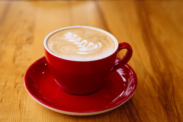 Aromatic coffee in a red cup with milk foam and latte art on a light wooden table.