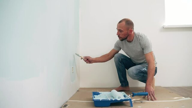 Caucasian man paints the wall with a brush Dad makes repairs in the room Quality work Side view