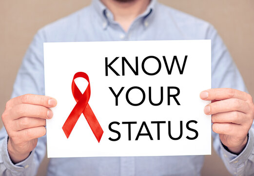 A man holding white sheet with a red ribbon on surface and text - know your status. Concept picture about hiv and aids pandemic in the World