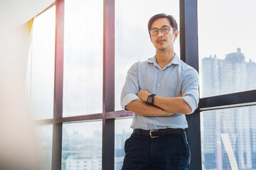 Portrait of business man standing next to office window with arms crossed.