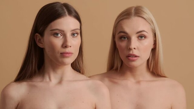 Confused young half-naked women are shrugging shoulders standing isolated over a beige background in the studio