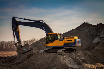 Obraz premium Large construction excavator yellow on a construction site in a quarry for quarrying. Yellow excavator on a construction site against blue sky.