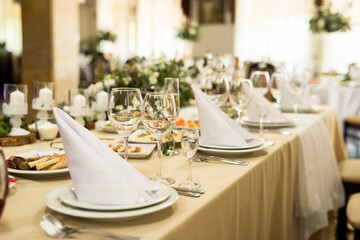 Close up of festive table setting with wine glasses, fresh flowers on beige tablecloth