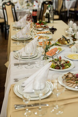 Close up of festive table setting with wine glasses, fresh flowers on beige tablecloth