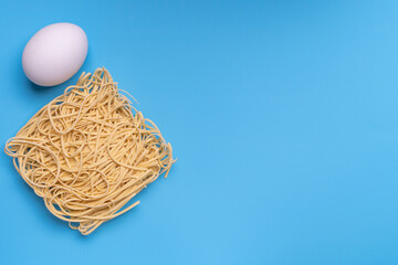 Instant noodles and white chicken egg on blue background. Copy-space. Top view