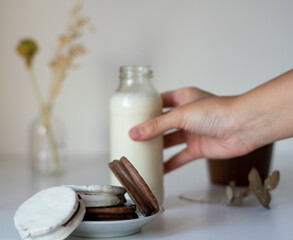 alfajores rellenos de dulce de leche cubiertos de chocolate con una botella de leche al lado, sobre una mesa blanca