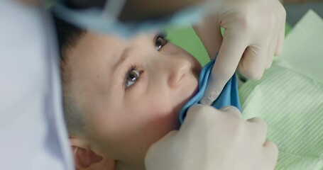 Close-up a little boy whom a medical worker is applying a rubber dam on the tooth.