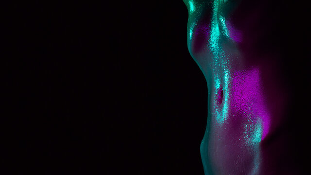Sexy wet tummy of a girl with water drops on her skin. Beautiful female waist in neon light