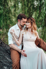 a guy and a girl are sitting together on a crooked tree on the steep bank