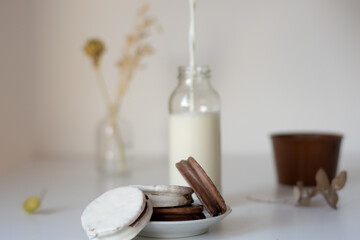 alfajores rellenos de dulce de leche cubiertos de chocolate con una botella de leche al lado, sobre una mesa blanca