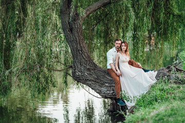 a guy and a girl are sitting together on a crooked tree on the steep bank