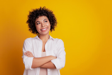 Portrait of positive smart girl folded arms look up empty space think isolated over yellow background