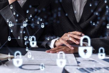 Two businesswomen working on the project to protect cyber security of international company. Padlock Hologram icons over the table with documents.