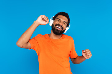 joyful african american man in wireless headphones listening music isolated on blue