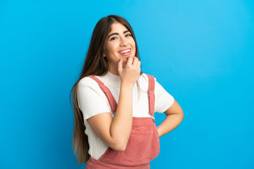 Young caucasian woman isolated on blue background looking up while smiling