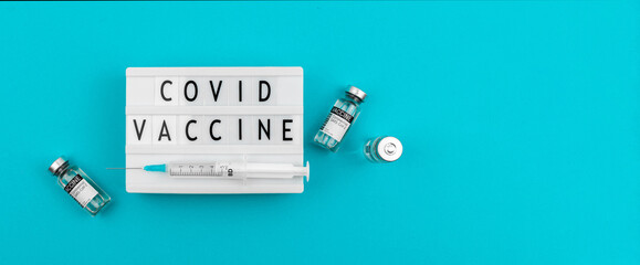 Covid-19 vaccine text message on the lightbox woth vaccine vials and medical syringe, copy space, banner photo