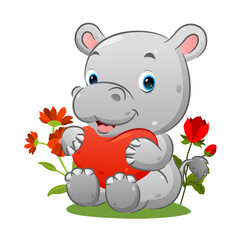 The cute hippopotamus is sitting on the grass and holding the heart balloon in the garden