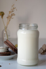 vaso o botella de leche sobre una mesa de color blanco, acompañado de alfajores tradicionales de argentina de dulce de leche con chocolate