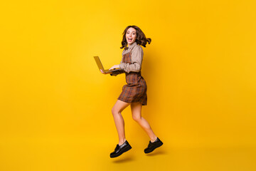 Fototapeta na wymiar Full size profile photo of optimistic brunette lady with laptop jump run wear shirt dress sneakers isolated on vivid yellow background