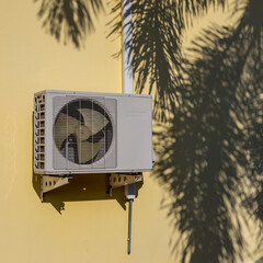 Air conditioner compressor near palm leaf shadow.