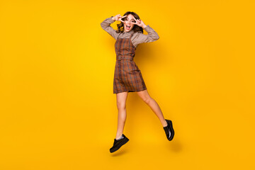 Full size photo of optimistic funny brunette lady jump show v-sign wear shirt dress sneakers isolated on vivid yellow background