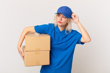 young pretty woman feeling puzzled and confused, scratching head. package delivering concept