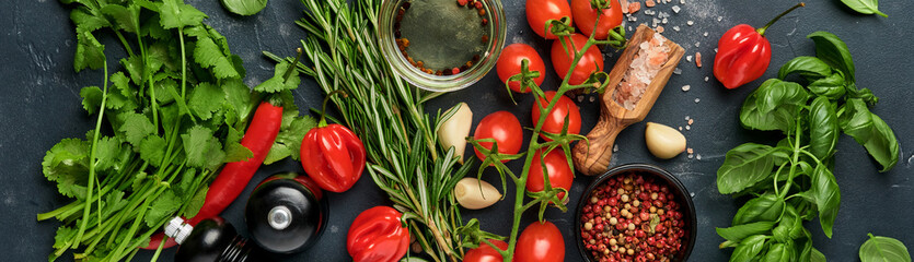 Food cooking background. Fresh rosemary, cilantro, basil, cherry tomatoes, peppers and olive oil, spices herbs and vegetables at black slate table. Bannr top view.