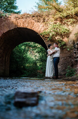 The bride and groom hug and kiss against the background of water and a stone arch