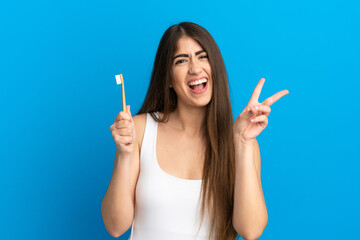 Obraz premium Young caucasian woman brushing teeth isolated on blue background smiling and showing victory sign