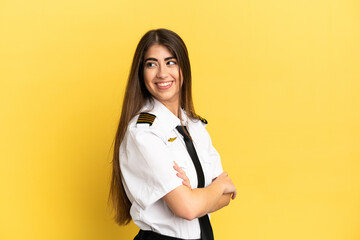 Airplane pilot isolated on yellow background with arms crossed and happy - obrazy, fototapety, plakaty