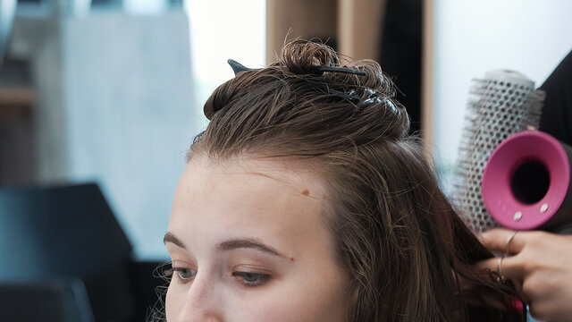 Hairdresser drying woman long hair using hairdryer and brush