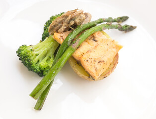 dish of fried river trout fillet with a complex side dish of broccoli, asparagus sprouts and mushroom sauce on white background