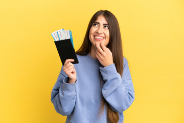 Naklejka premium Young caucasian woman holding a passport isolated on yellow background looking up while smiling