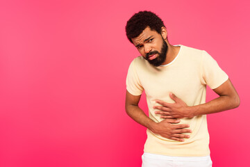 displeased african american man suffering from stomach ache isolated on pink