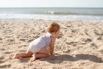 Fototapeta na wymiar Small girl crawls on sand at beach near the sea